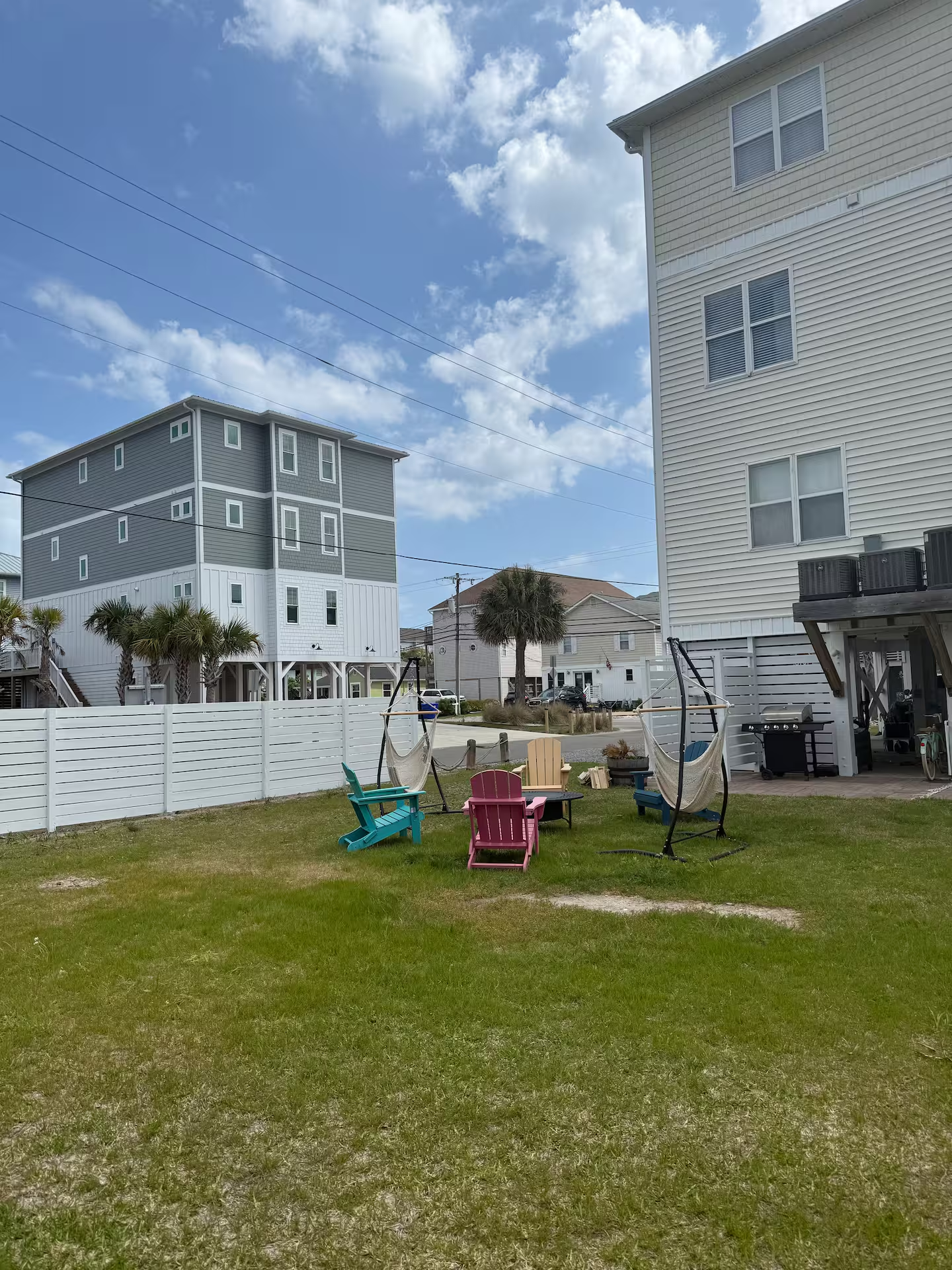 Spacious backyard at Shore Thing Y’all with colorful Adirondack chairs, hammocks, and a grill